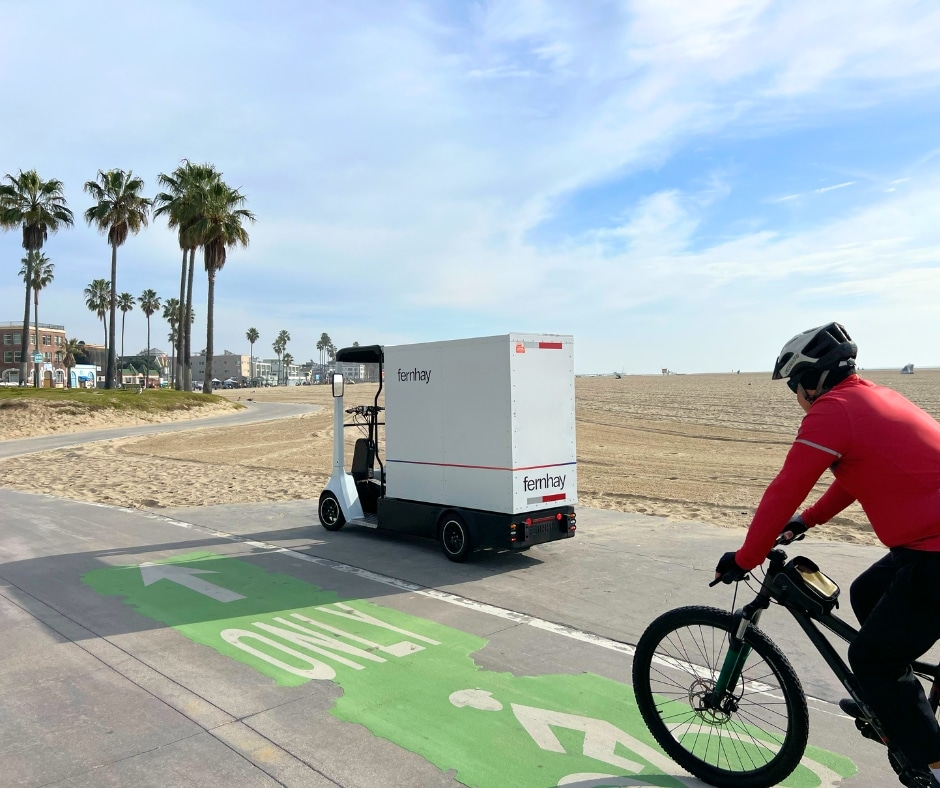 Fernhay eQuad driving in the bike lane in Santa Monica, Los Angeles, representing micromobility urban infrastructure with palm trees, ocean, and a cyclist nearby